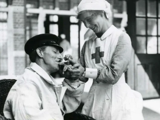A British Red Cross nurse lighting a cigarette for a patient